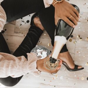 Среди блестящего декора рука с бутылкой шампанского и фужером. фото